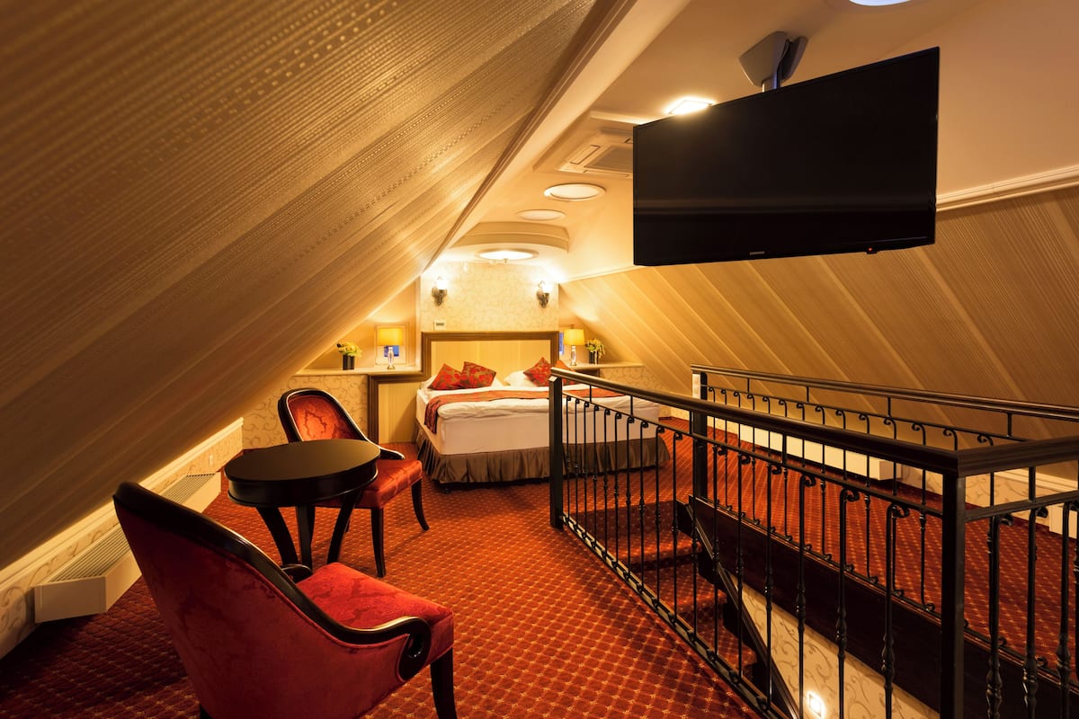 Quarto de hotel com cama, escrivaninha, cadeira, televisão e escada.
