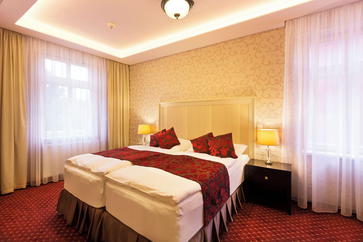 Quarto de hotel com uma cama grande, duas mesas de cabeceira com luminárias, uma cabeceira e um papel de parede estampado.