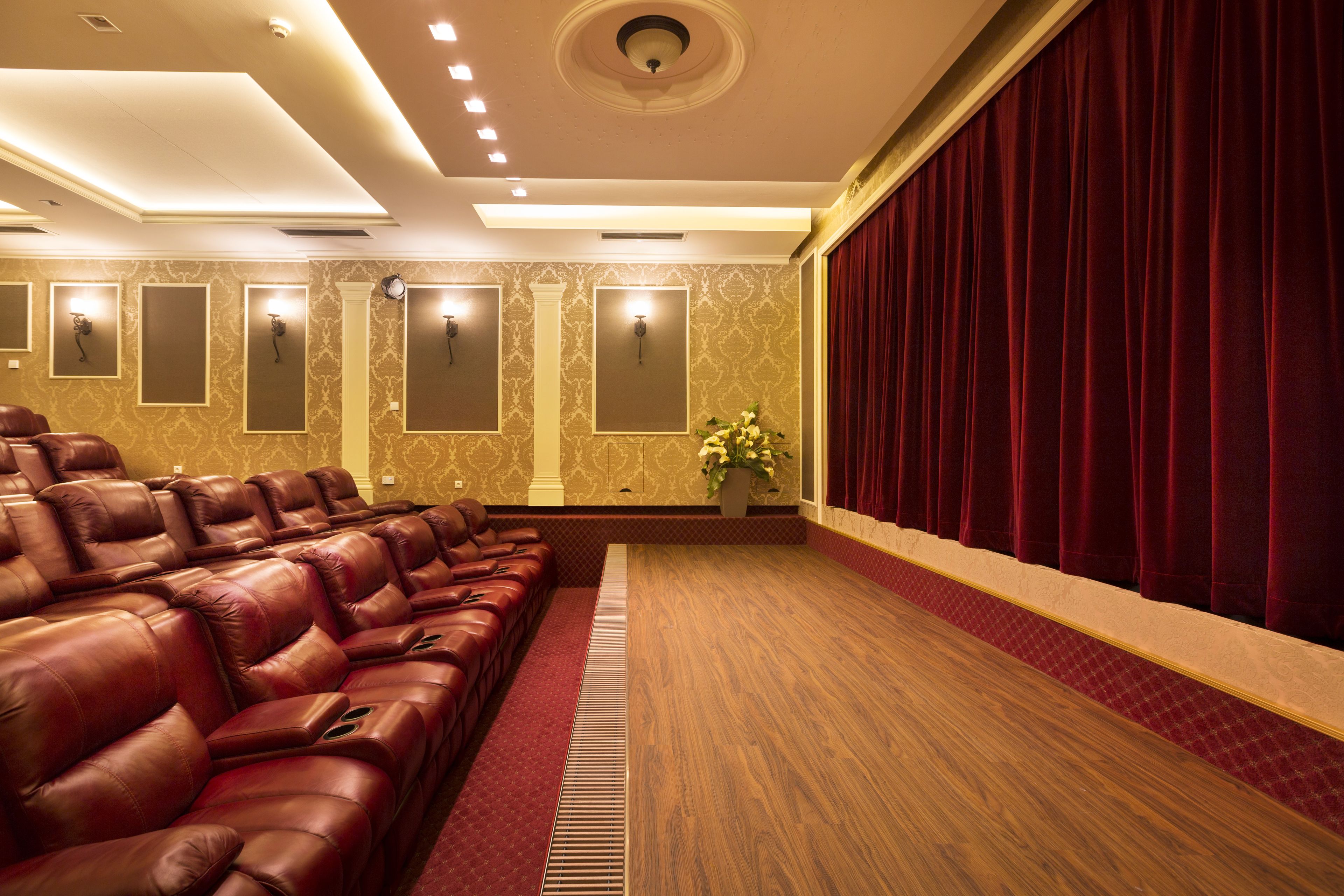 Um teatro com fileiras de assentos de couro, um pano de fundo de cortina vermelha e arandelas nas paredes.