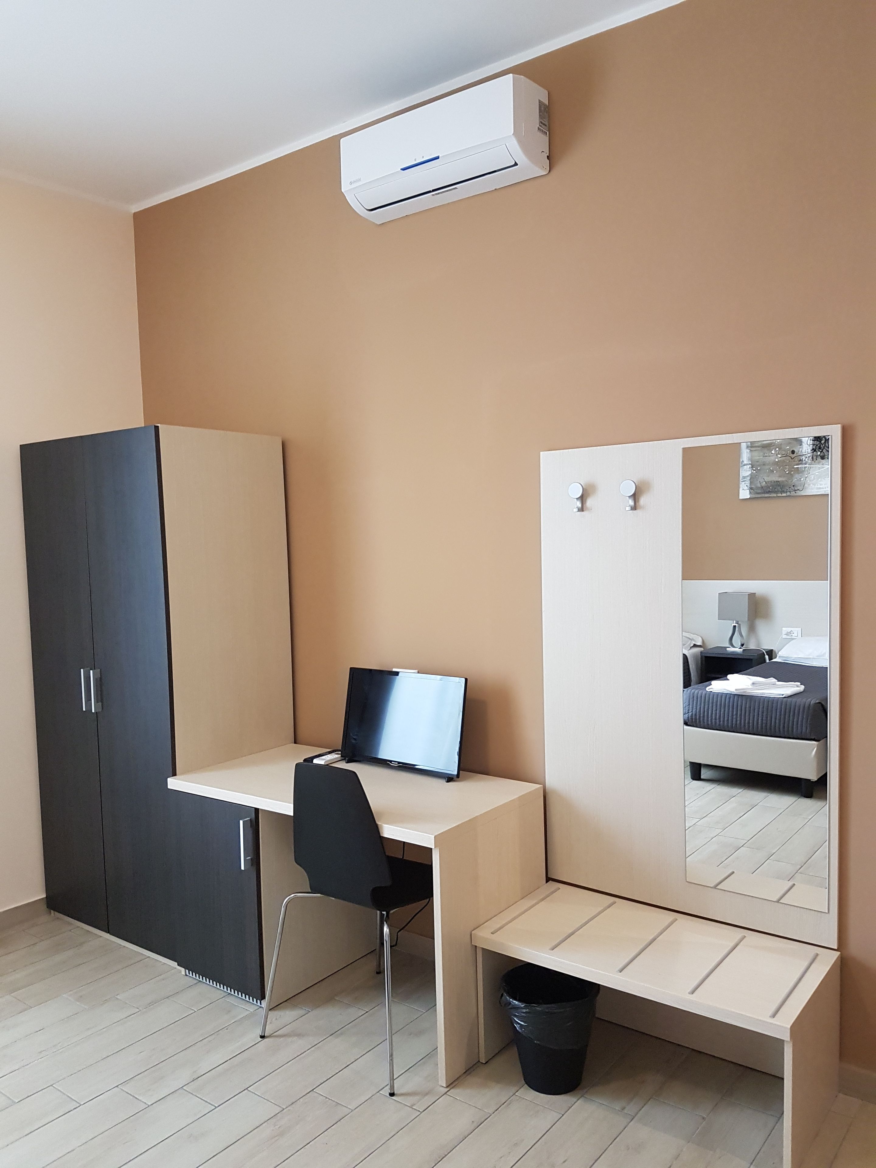 A room with a desk, chair, wardrobe, and a bed with a mirror.