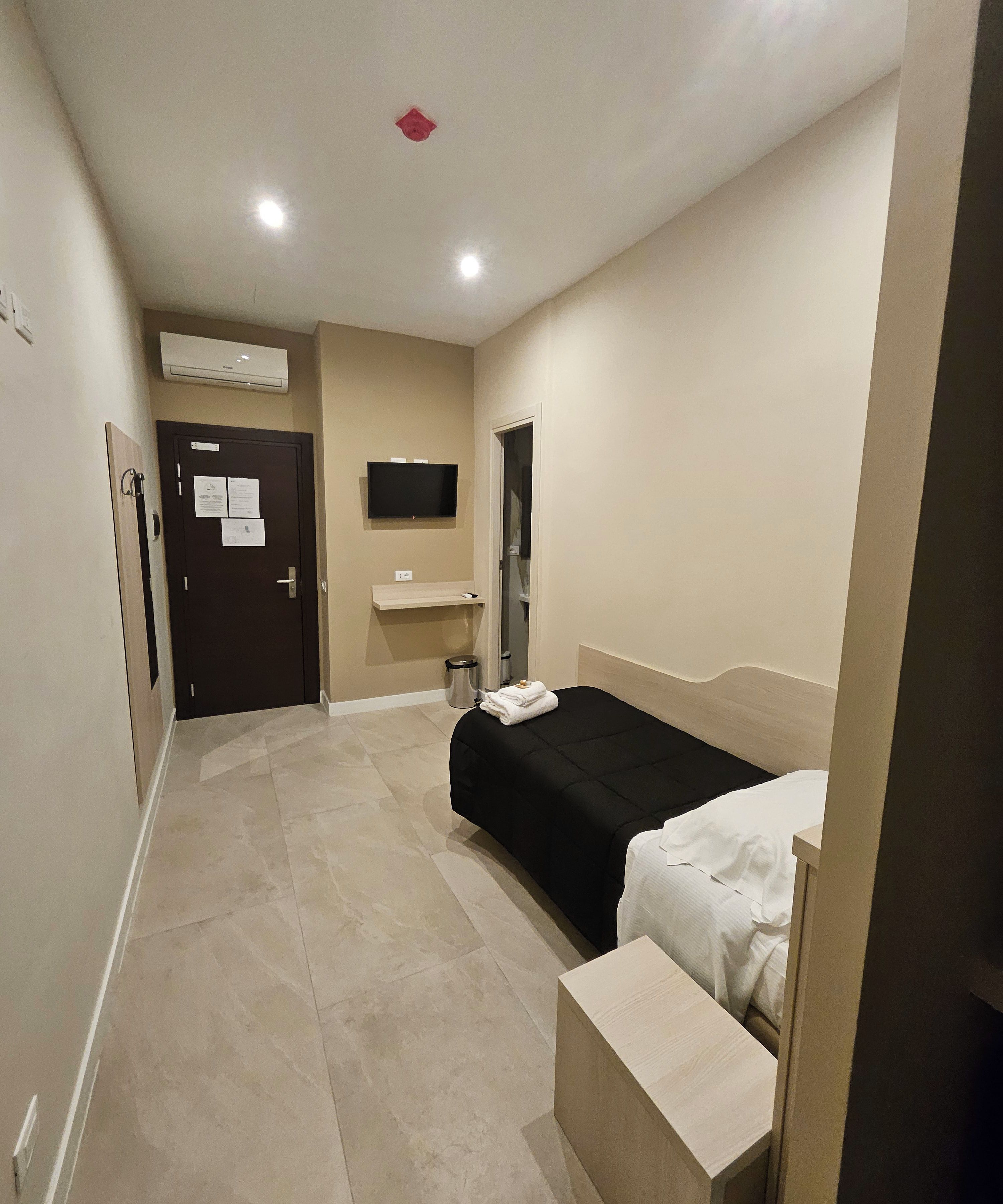 A hotel room with a bed, a small bedside table, a TV mounted on the wall, and a door leading to a bathroom.