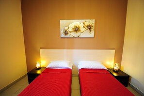 A hotel room with two beds, each with a red bedspread and white pillows, flanked by nightstands with lamps. A floral artwork is displayed on the wall above the beds. - Hotel Mosaic Central Rome (Rome)