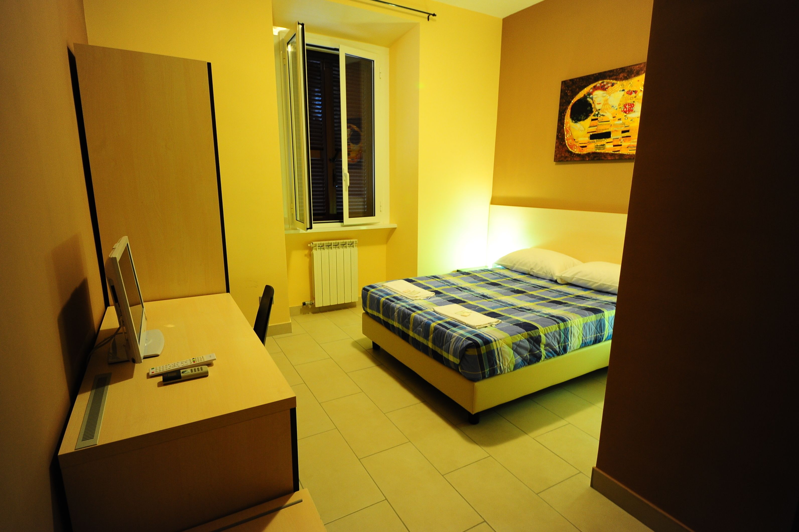 Une chambre à coucher avec un lit, un bureau avec un ordinateur, une fenêtre et un radiateur.