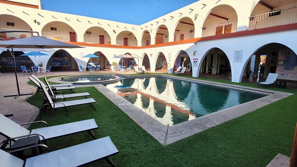 Un área de piscina con sillas de descanso, una piscina y un edificio con balcones arqueados.