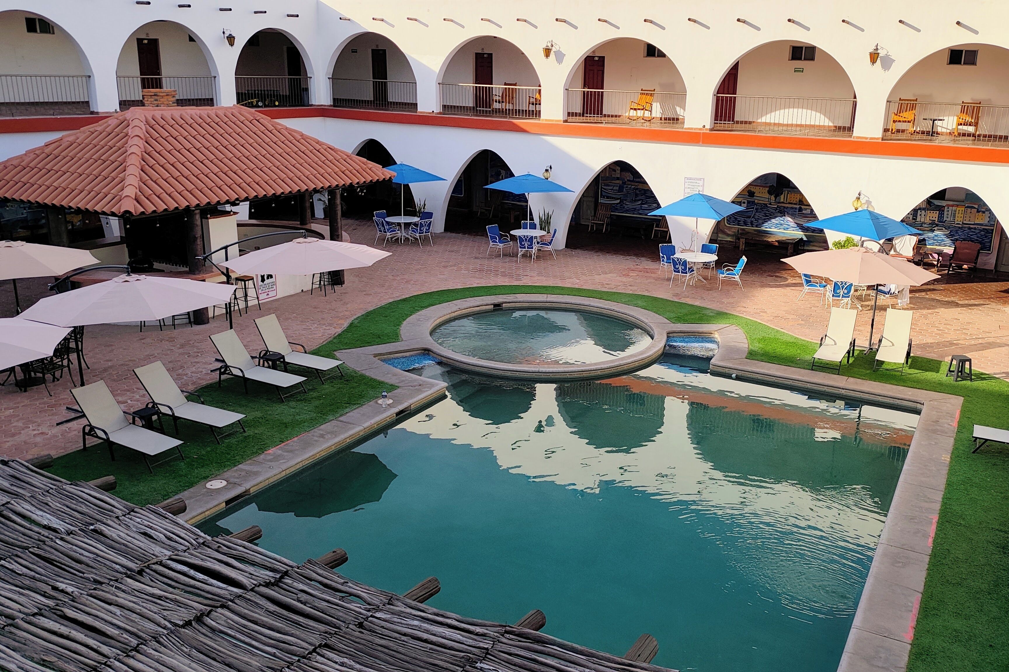 Une cour avec une piscine, des sièges extérieurs et un espace abrité avec des parasols.