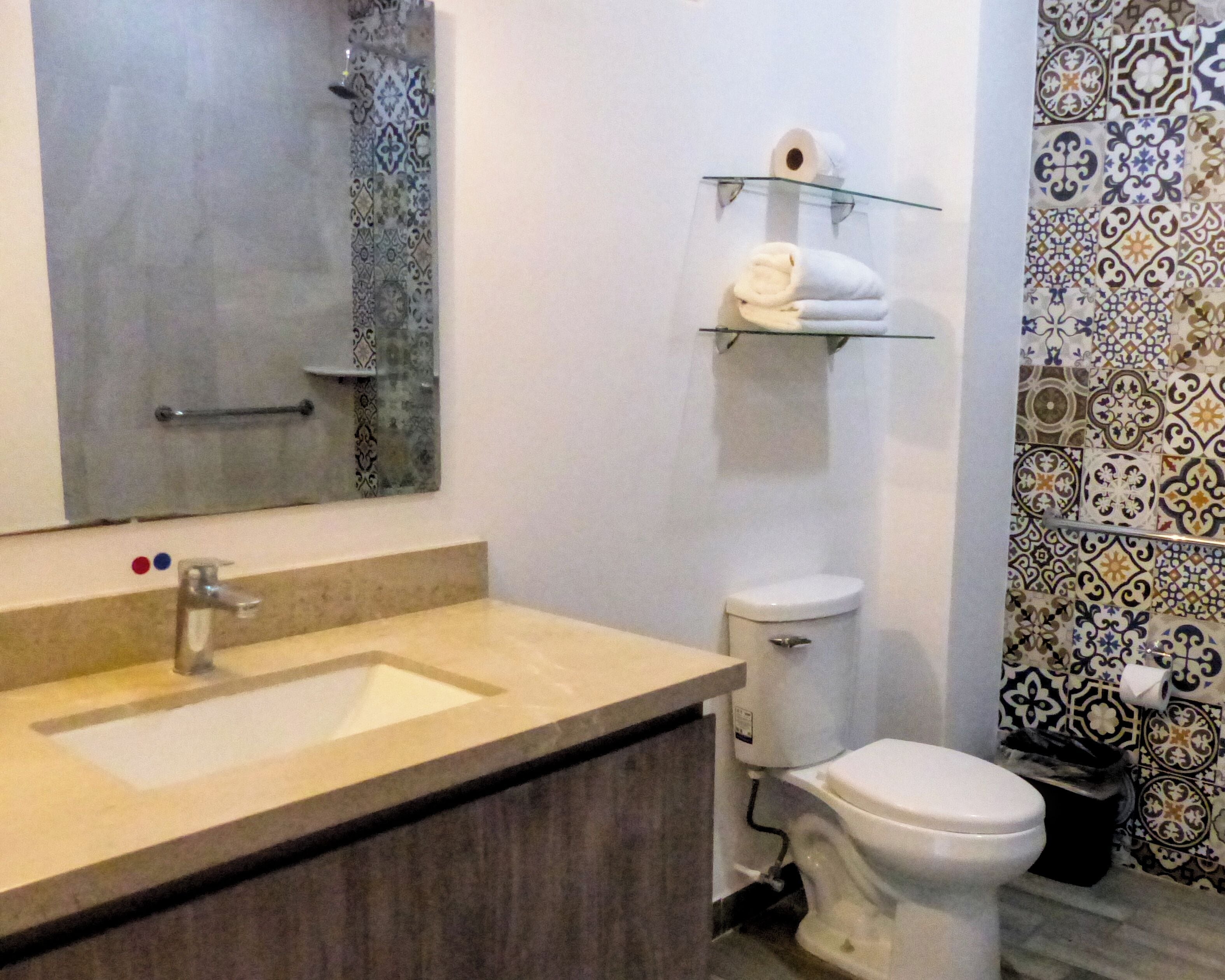 Un baño con lavamanos, espejo, inodoro y azulejos estampados.