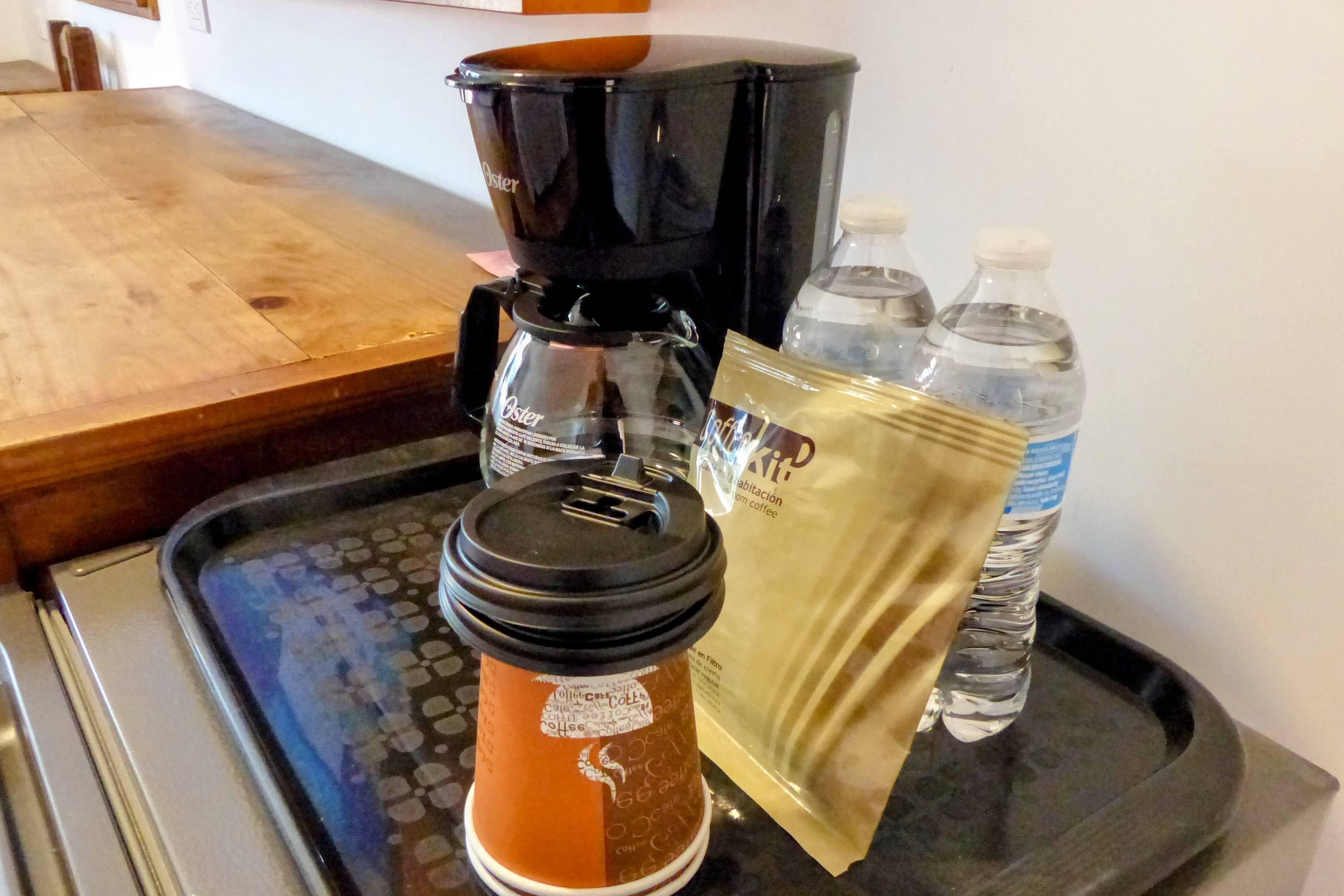 A coffee maker, a disposable coffee cup, and two water bottles on a tray.