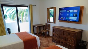 Habitación de hotel con dos camas, un aparador de madera, un televisor en la pared y vistas a palmeras por la ventana.