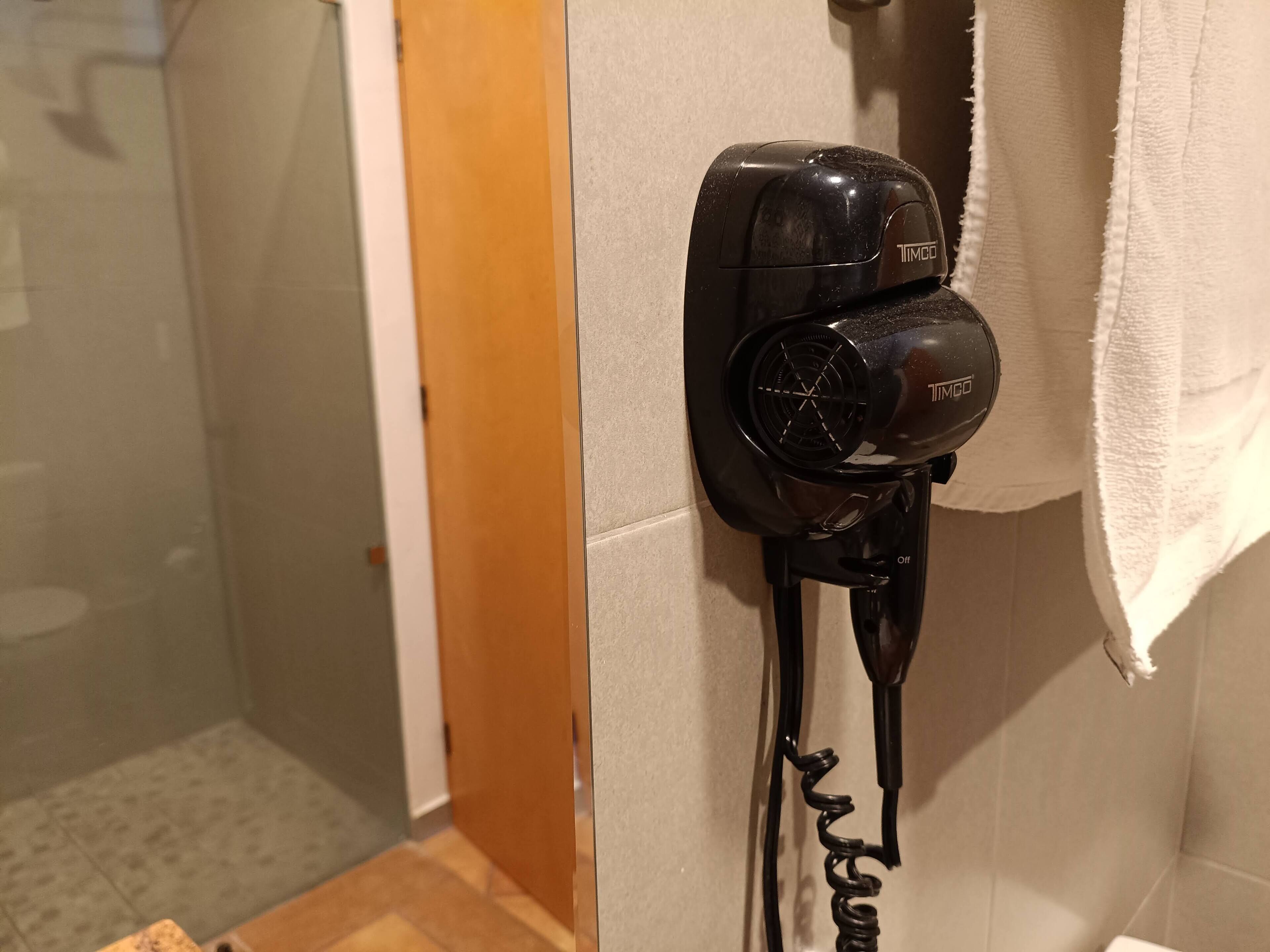 A black hairdryer mounted on a wall with a visible power cord.
