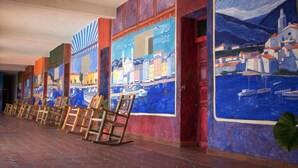 A hallway with colorful murals depicting coastal scenes and a row of wooden chairs. - Hotel Hacienda Bugambilias La Paz & Centro de Convenciones (La Paz)