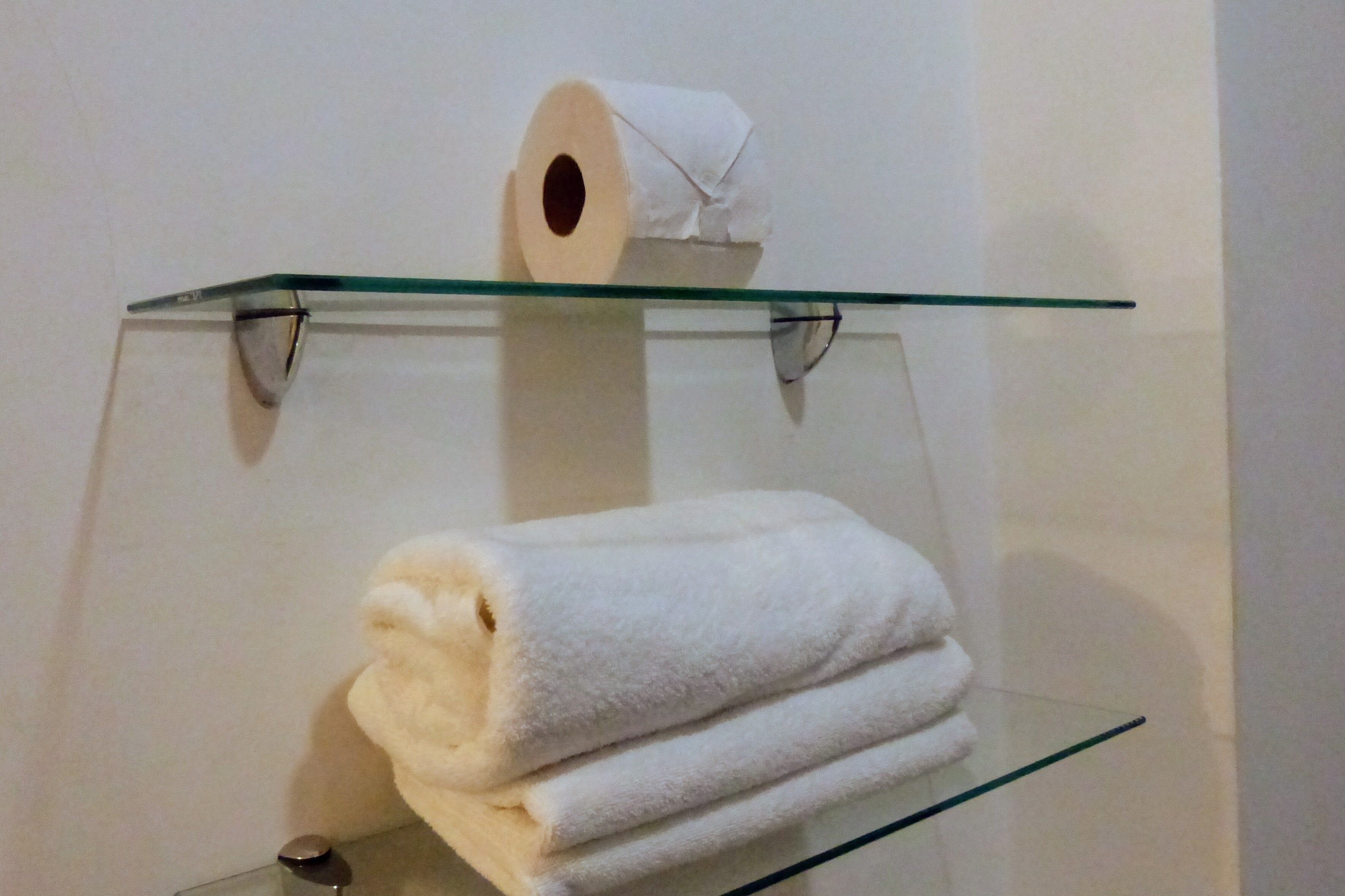 A glass shelf with a roll of toilet paper and a folded white towel.
