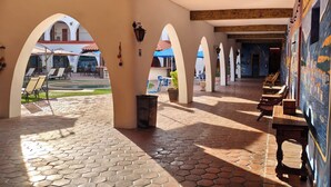 Un espacio al aire libre techado con suelo de baldosas hexagonales, bancos de madera y arcos.