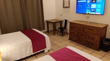 A hotel room with two beds, a wooden dresser, a desk, a chair, a television mounted on the wall, and a window with curtains.