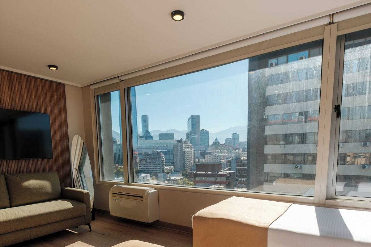 Una habitación de hotel moderna con un ventanal grande, un sofá, una cama y un televisor de pantalla plana.