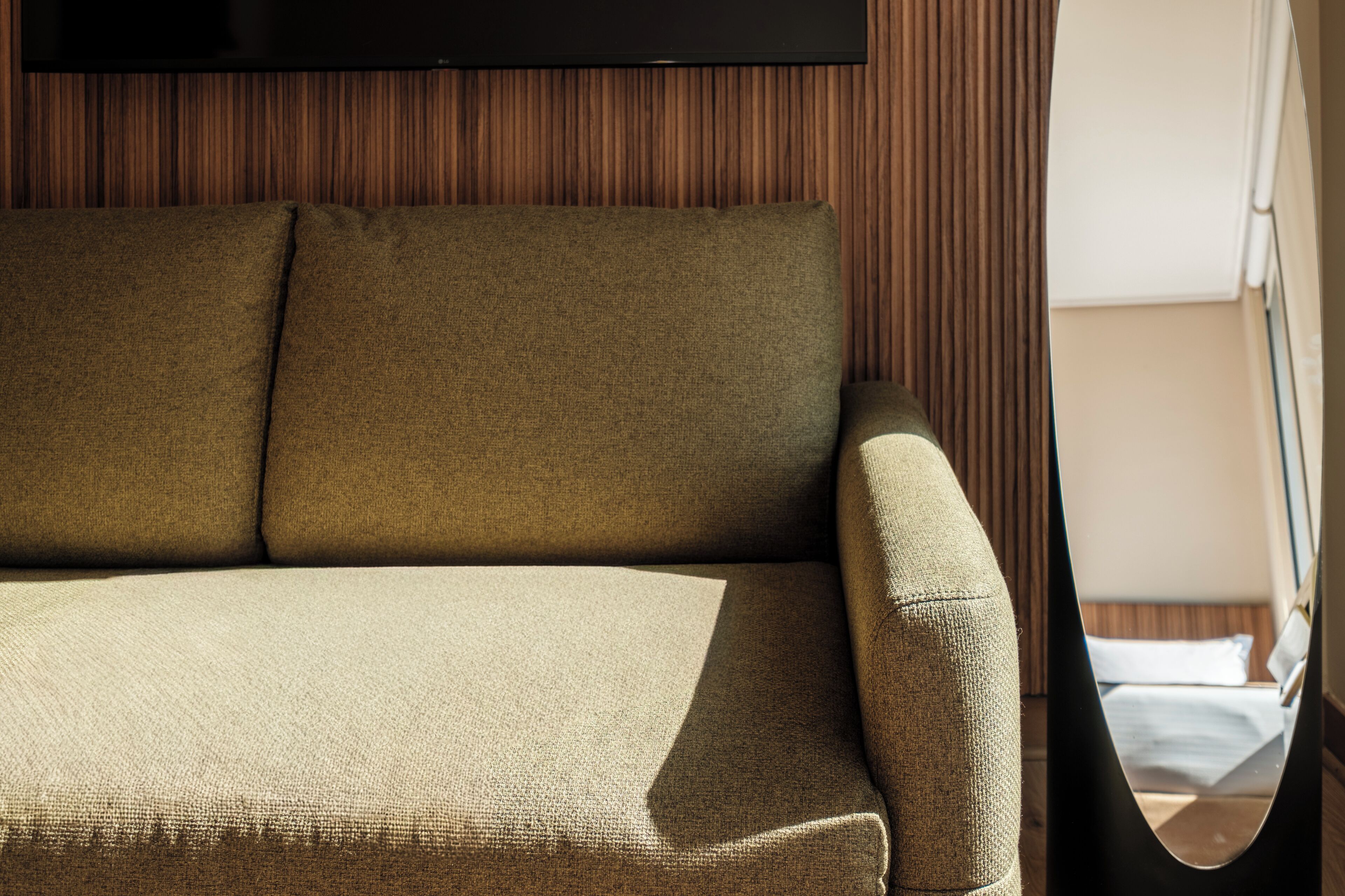 A sofa with a cushion, a television mounted on the wall, and a window with blinds.