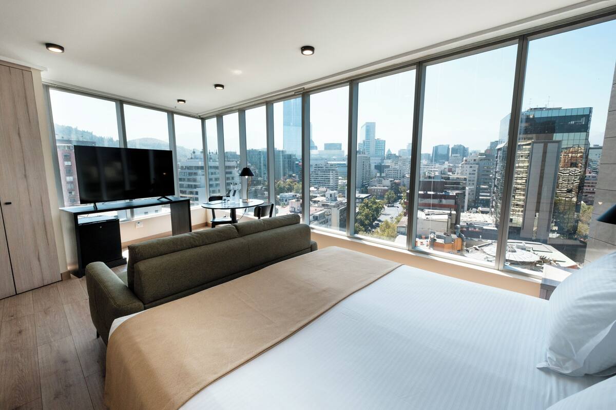 Una habitación de hotel moderna con una cama grande, un sofá, un televisor y vistas a la ciudad.