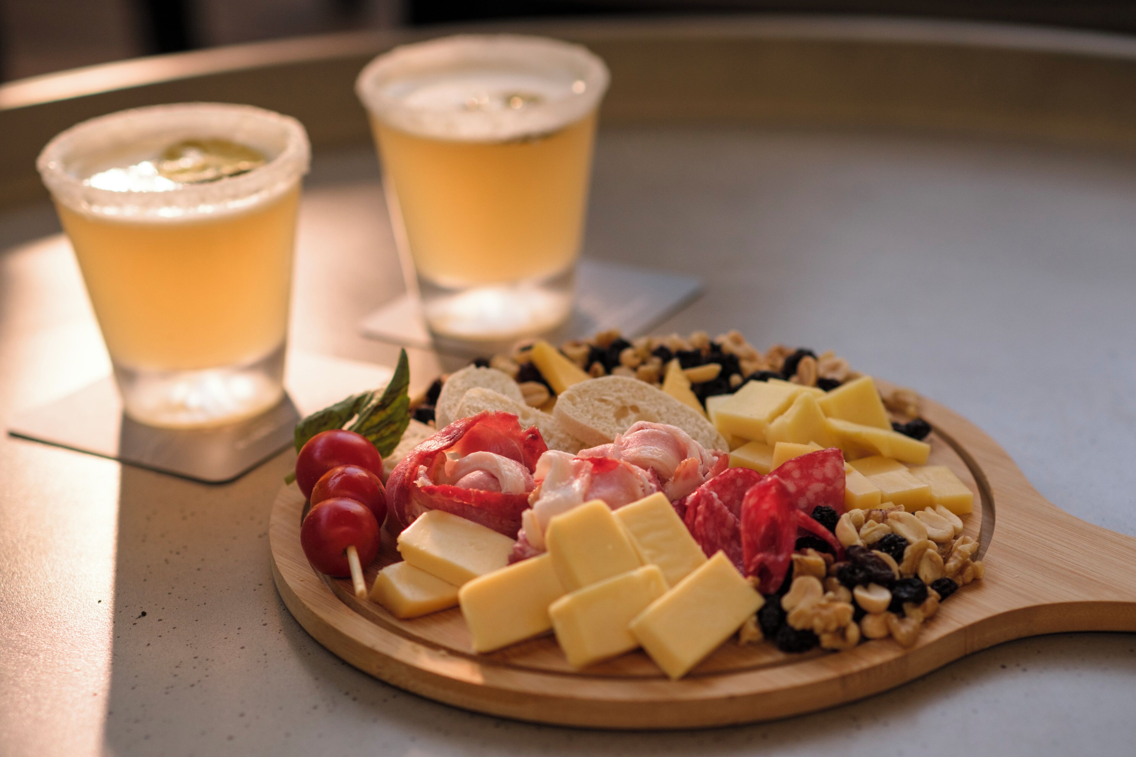 Une planche en bois garnie de fromage, de noix et de charcuteries, accompagnée de deux verres de bière, posée sur une table.