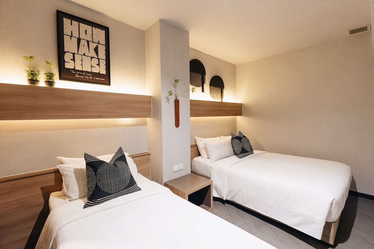 Habitación de hotel con dos camas, cabecero de madera, una obra de arte colgada en la pared y una planta pequeña en la mesita de noche.