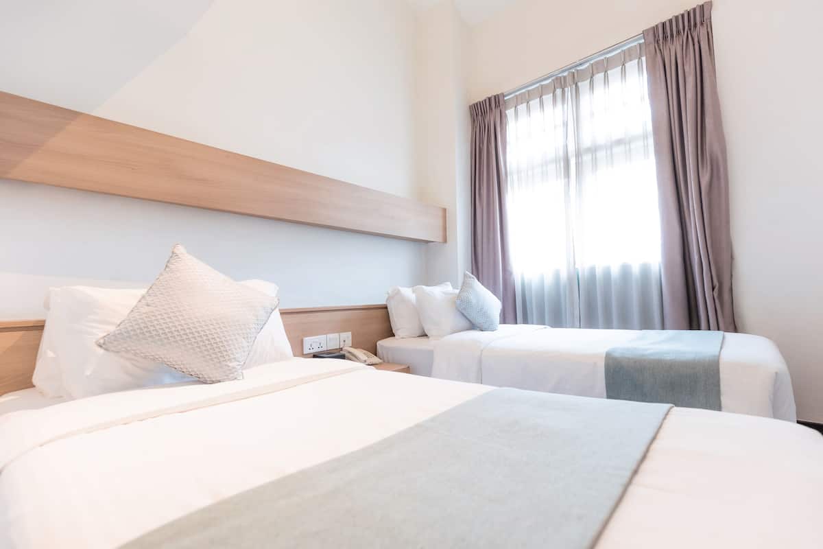 A hotel room with two beds, a wooden headboard, a telephone, and a window with curtains.