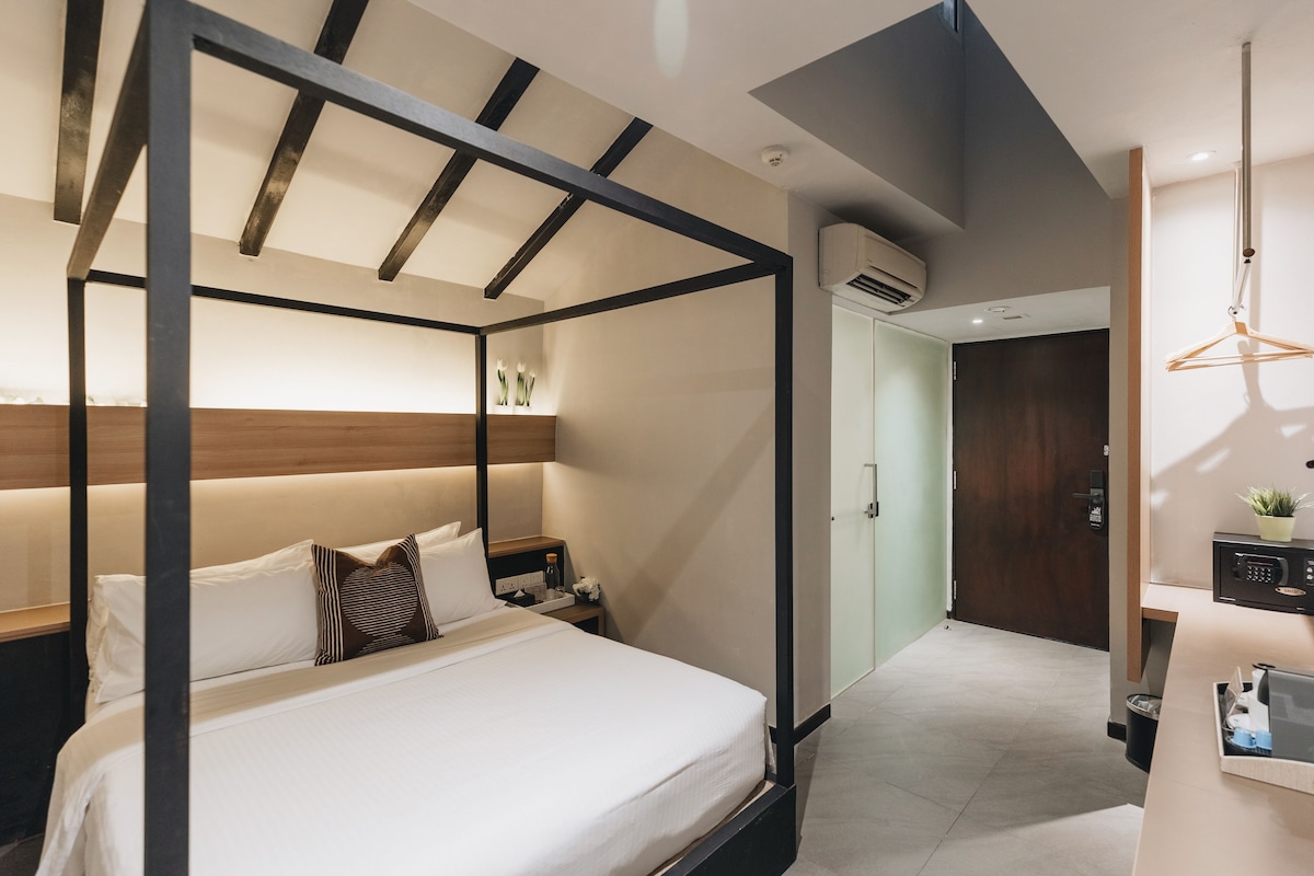 Un dormitorio moderno con cama con dosel, una mesita de noche con lámpara y una planta pequeña en la mesita.