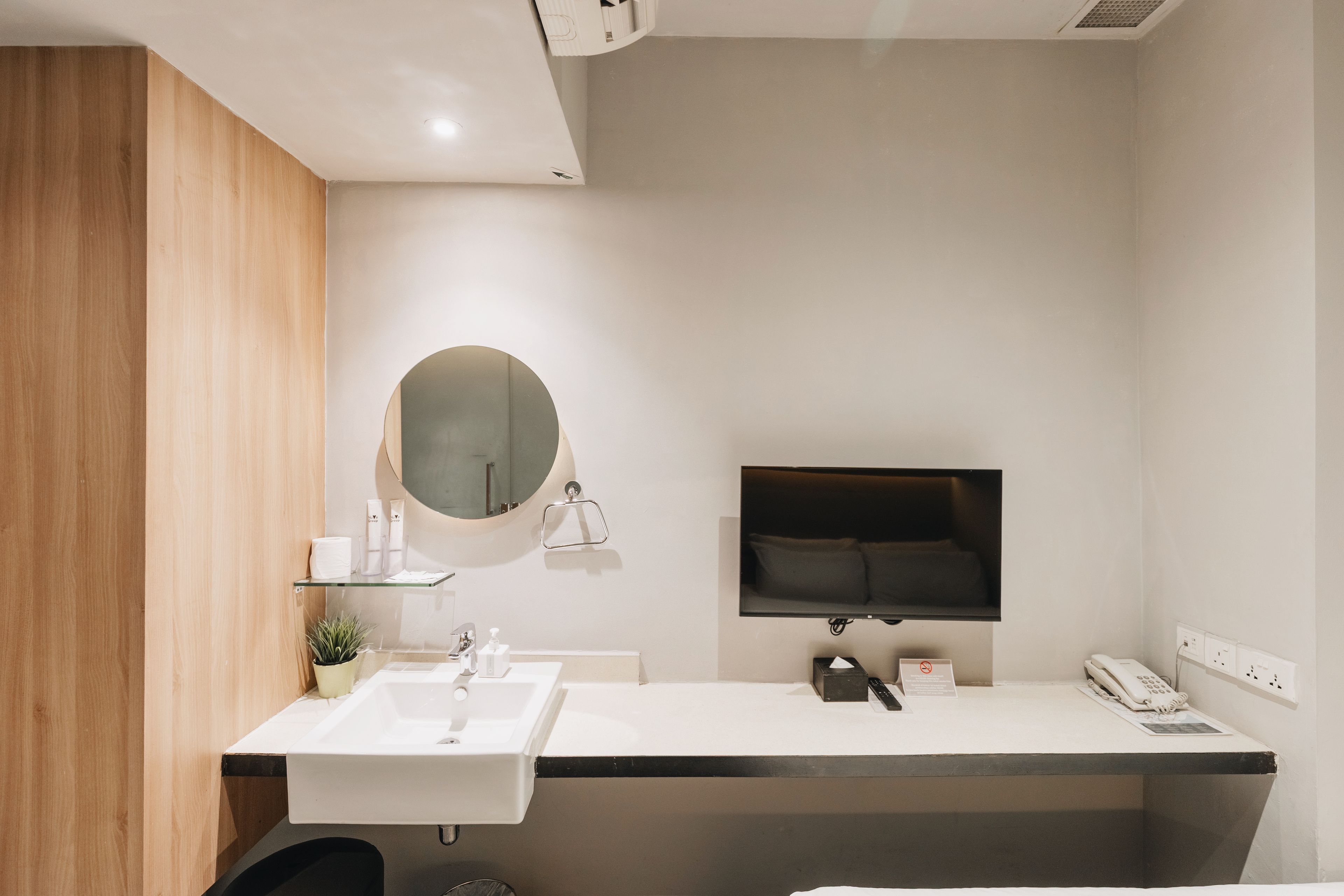 Ein modernes Badezimmer mit einem weißen Waschbecken, einem Spiegel und einem flachbildfernseher an der Wand.