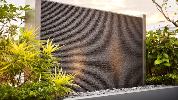 A modern outdoor wall with a textured surface, surrounded by various plants and a gravel border. - Hotel Nuve (Singapore)