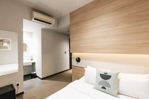 A modern hotel room with a wooden headboard, a bed with white linens, a bedside table, and a wall-mounted air conditioner. - Hotel Nuve (Singapore)
