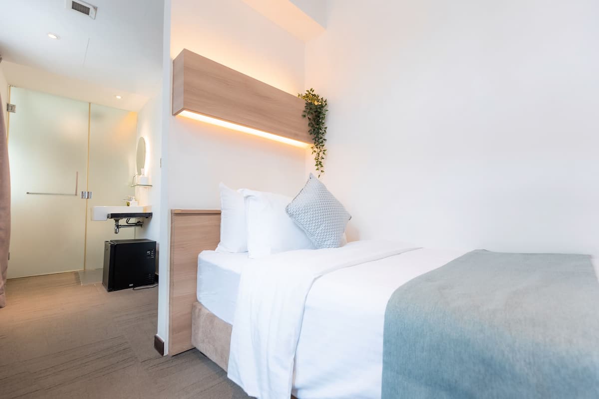 A modern hotel room with a bed, bedside table, and a small desk with a lamp.