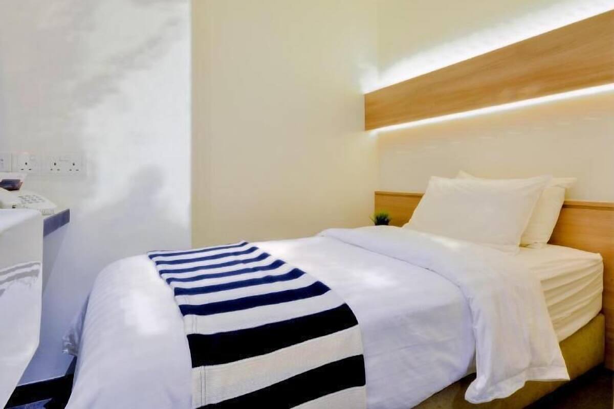 A hotel room with a bed, bedside table, and a wall socket.