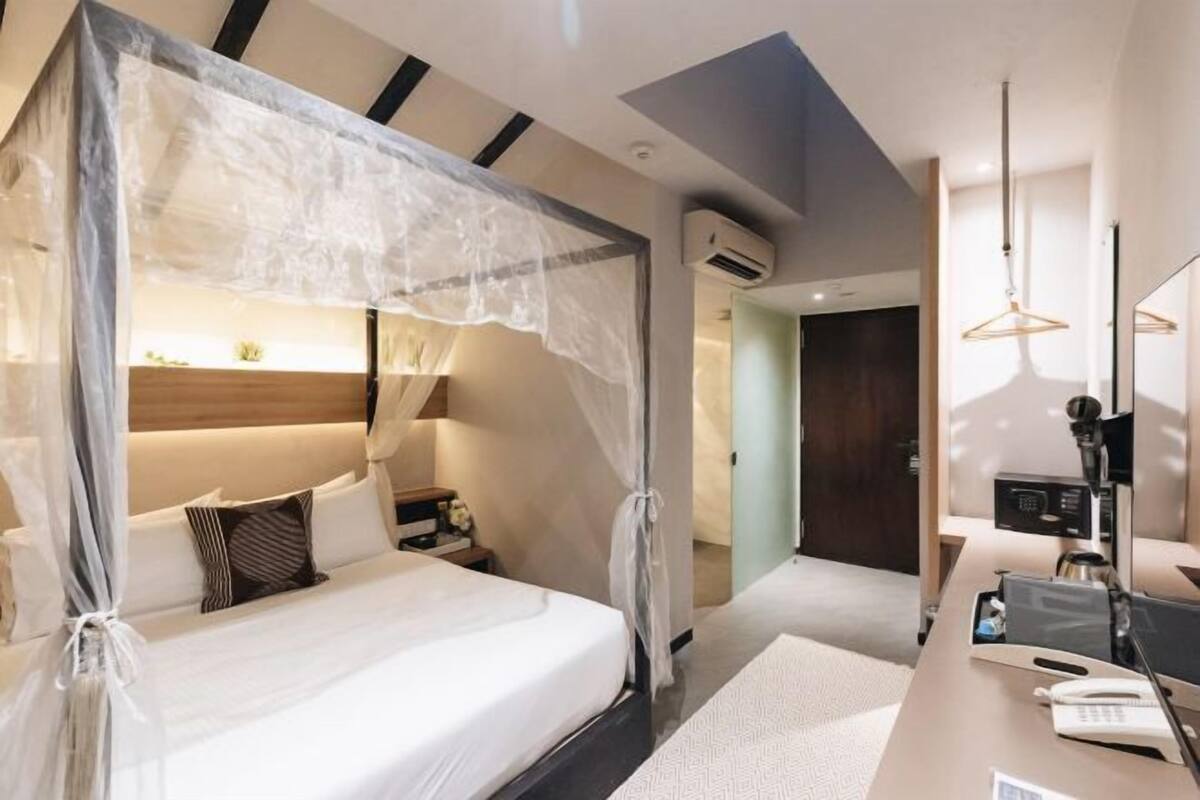 A modern hotel room with a bed, bedside table, desk, and chair.