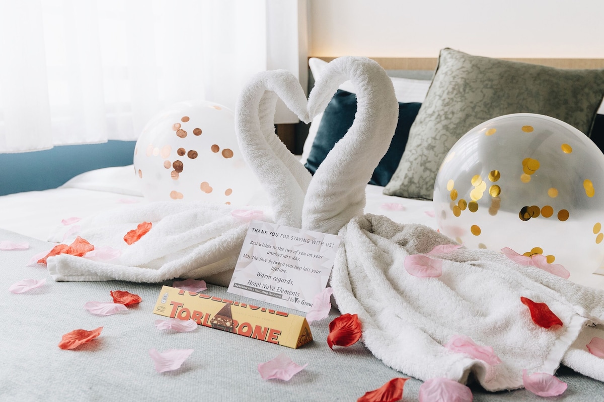 Una cama con una toalla con forma de cisne, una nota de agradecimiento y una barra de chocolate.