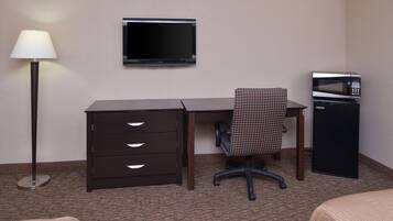 A hotel room with a desk, chair, TV, microwave, and a lamp.