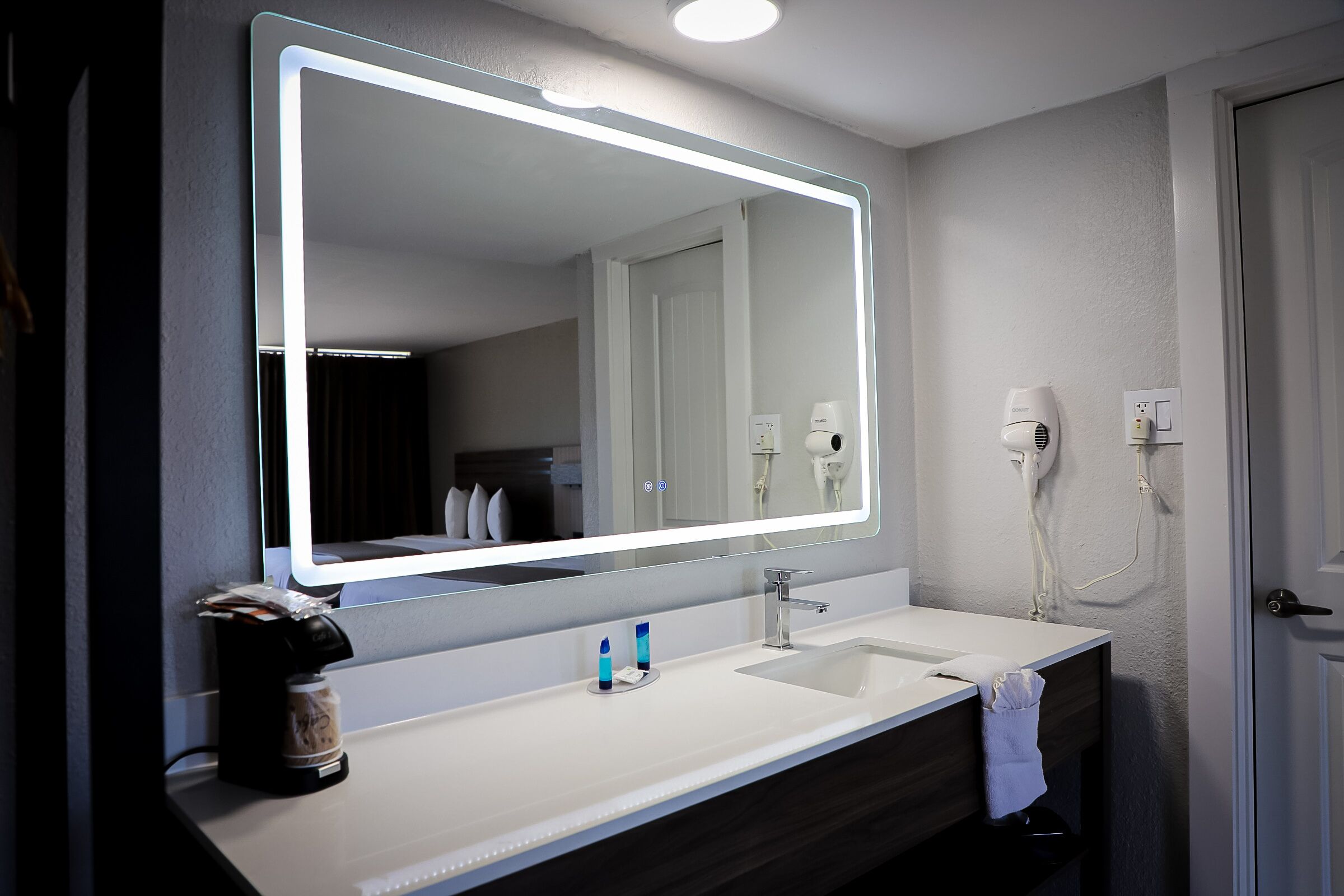 A bathroom with a large mirror, two sinks, a towel rack, and a hairdryer.