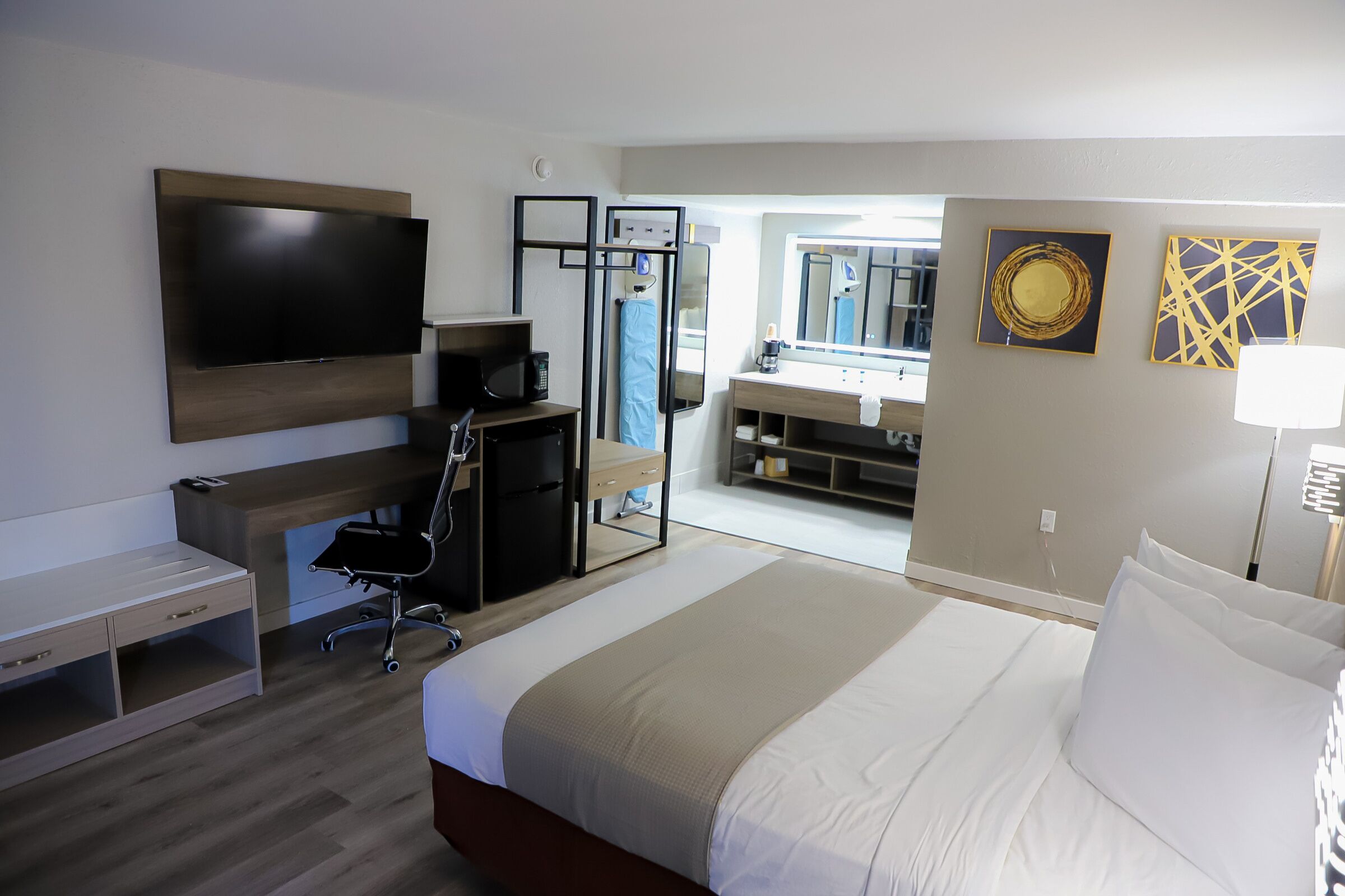 Une chambre d’hôtel avec un lit, un bureau, une télévision, un miroir et une salle de bain visible à travers une porte ouverte.