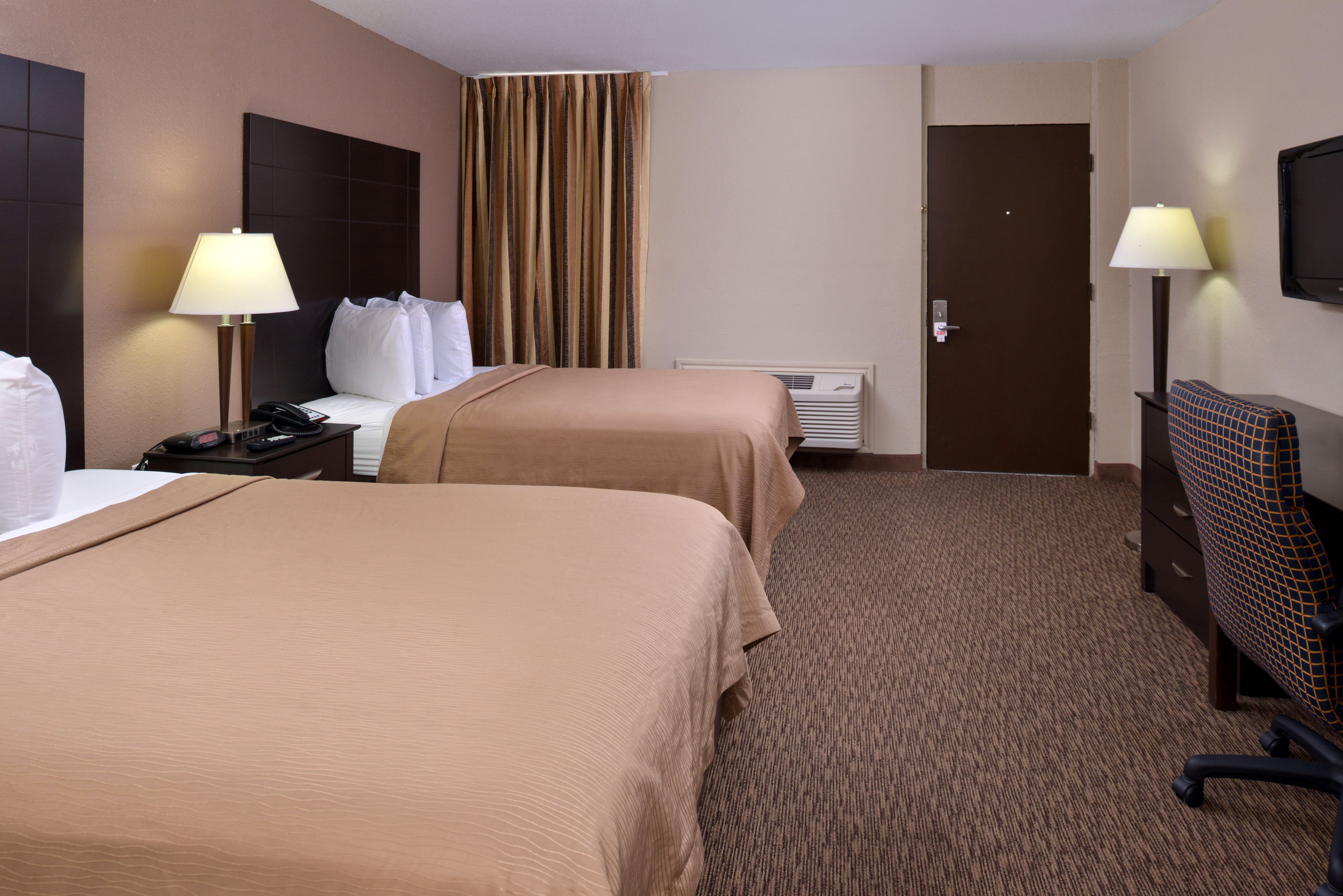 Habitación de hotel con dos camas, un escritorio, una silla, una lámpara, un calentador y una puerta.