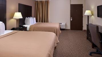 Habitación de hotel con dos camas, un escritorio, una silla, una lámpara, un calentador y una puerta.