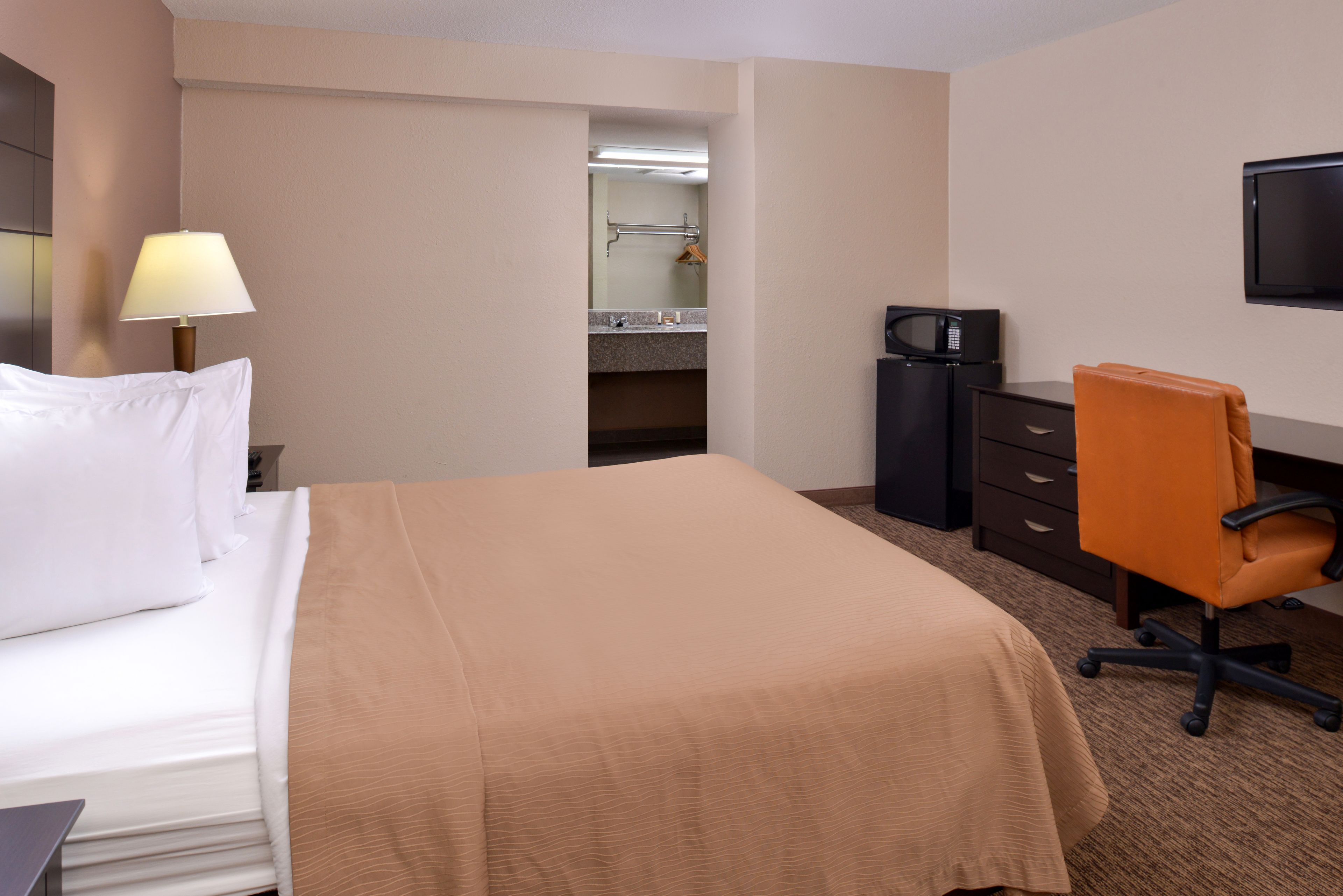 A hotel room with a bed, a desk, a chair, a TV, a microwave, and a bathroom visible through an open door.