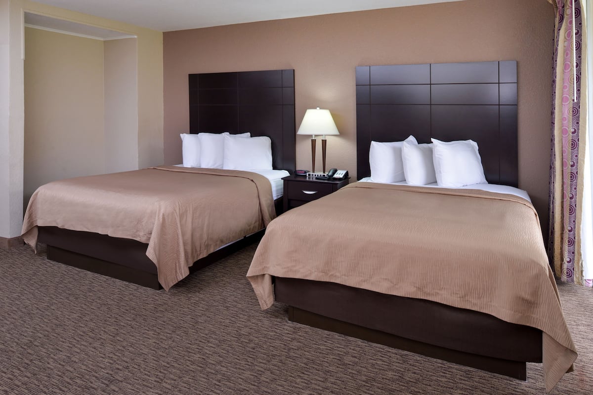 A hotel room with two beds, a nightstand with a lamp, and a large headboard.