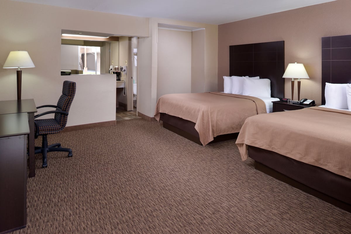 A hotel room with two beds, a desk, a chair, a bathroom, and a mirror.