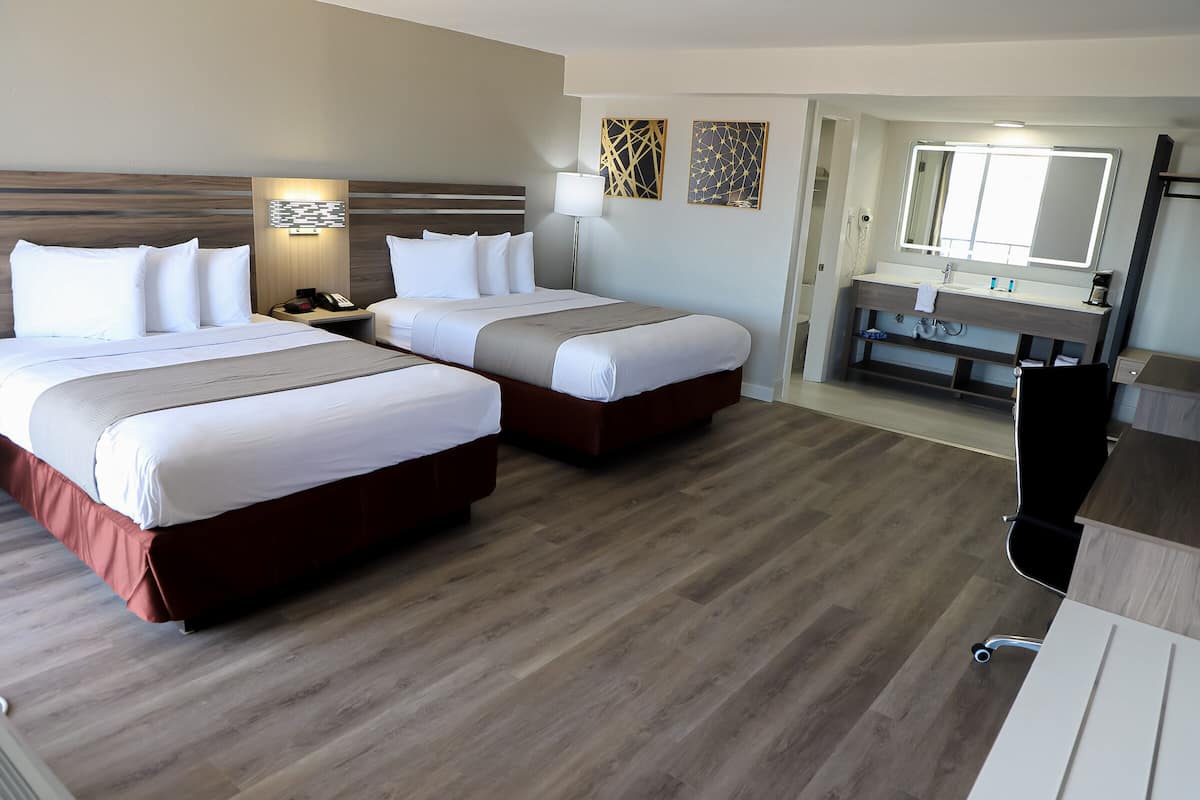 A hotel room with two beds, a desk, a chair, a vanity with a mirror, and a phone.