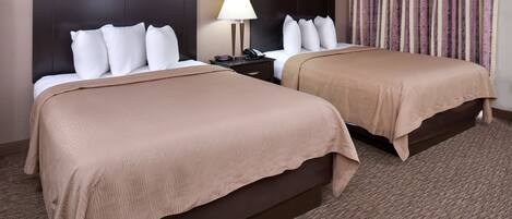 Habitación de hotel con dos camas, una mesita de noche con lámpara y cortina estampada.