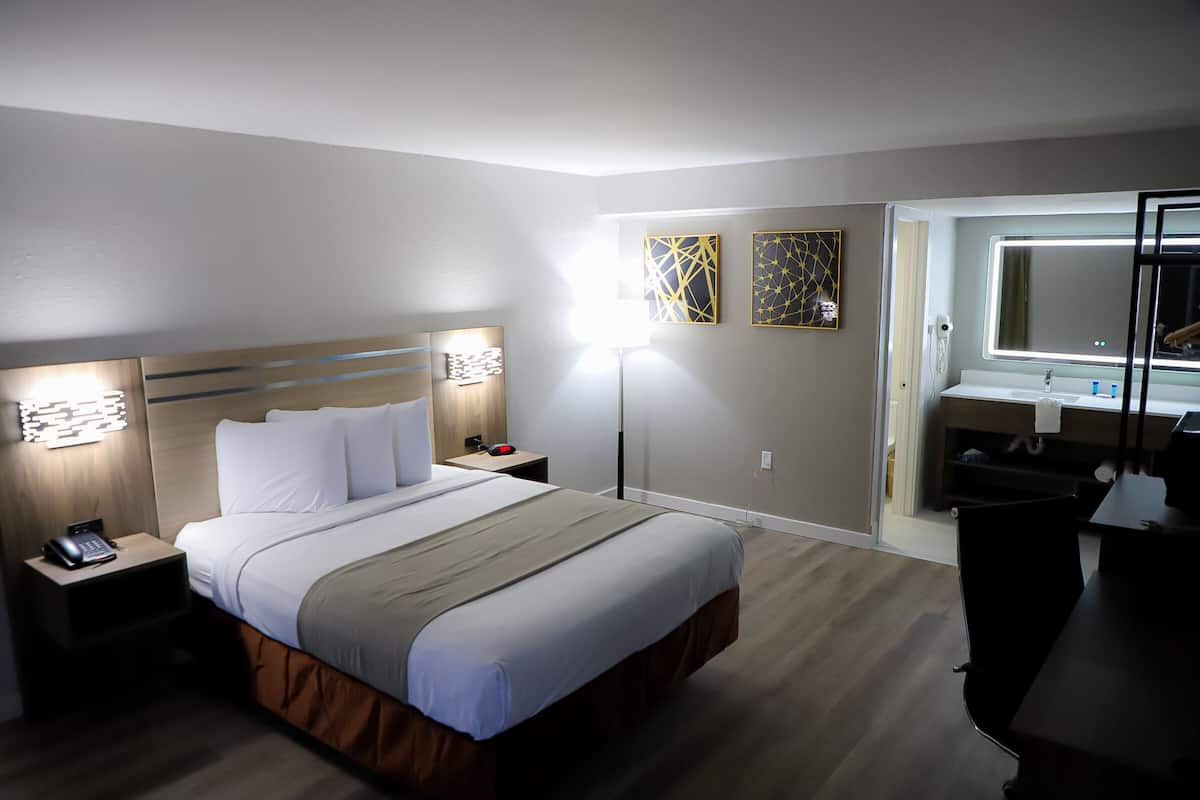 A hotel room with a bed, bedside tables, a desk, a mirror, and artwork on the walls.