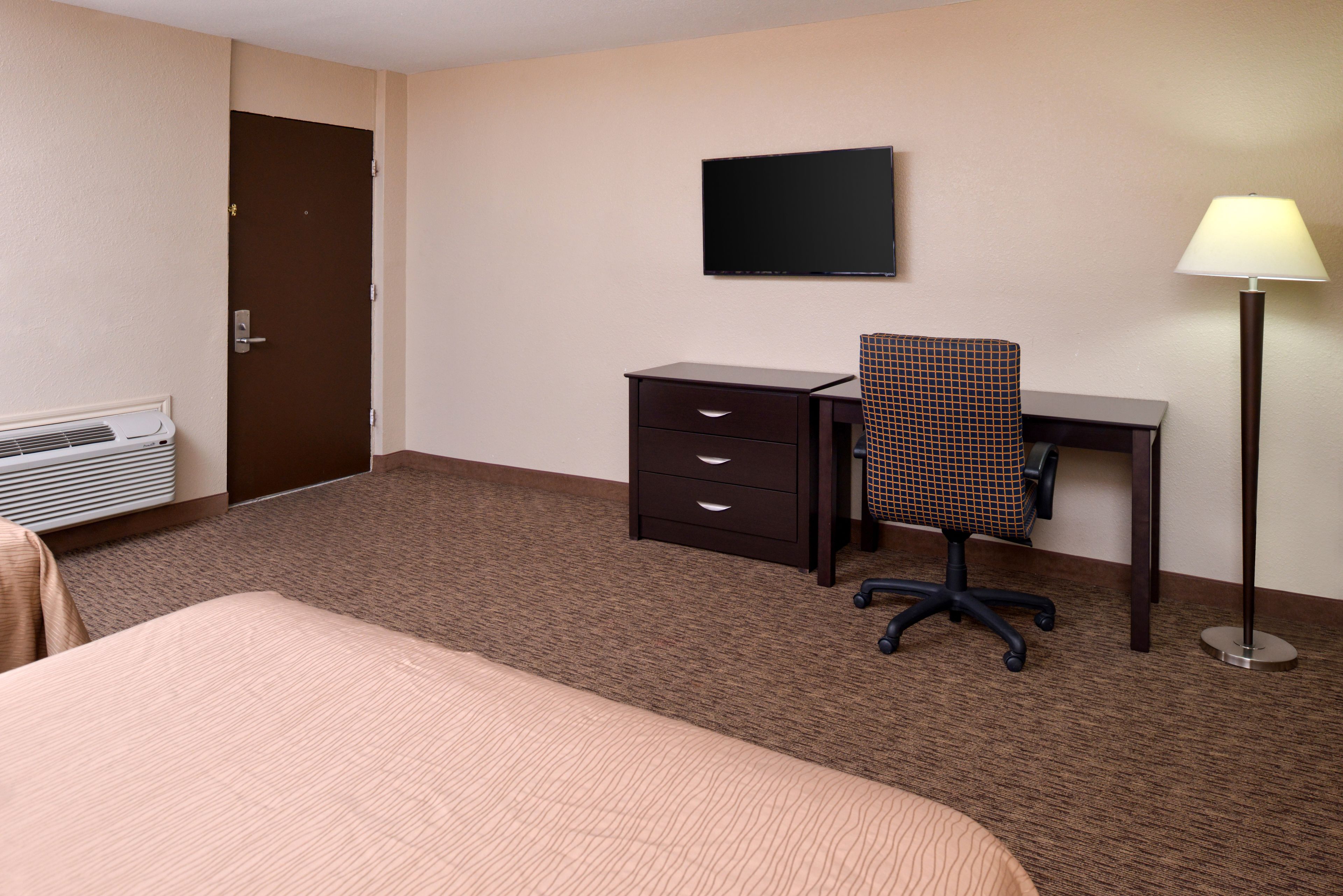 Una habitación de hotel con cama, escritorio con silla, televisor, lámpara y calefactor.