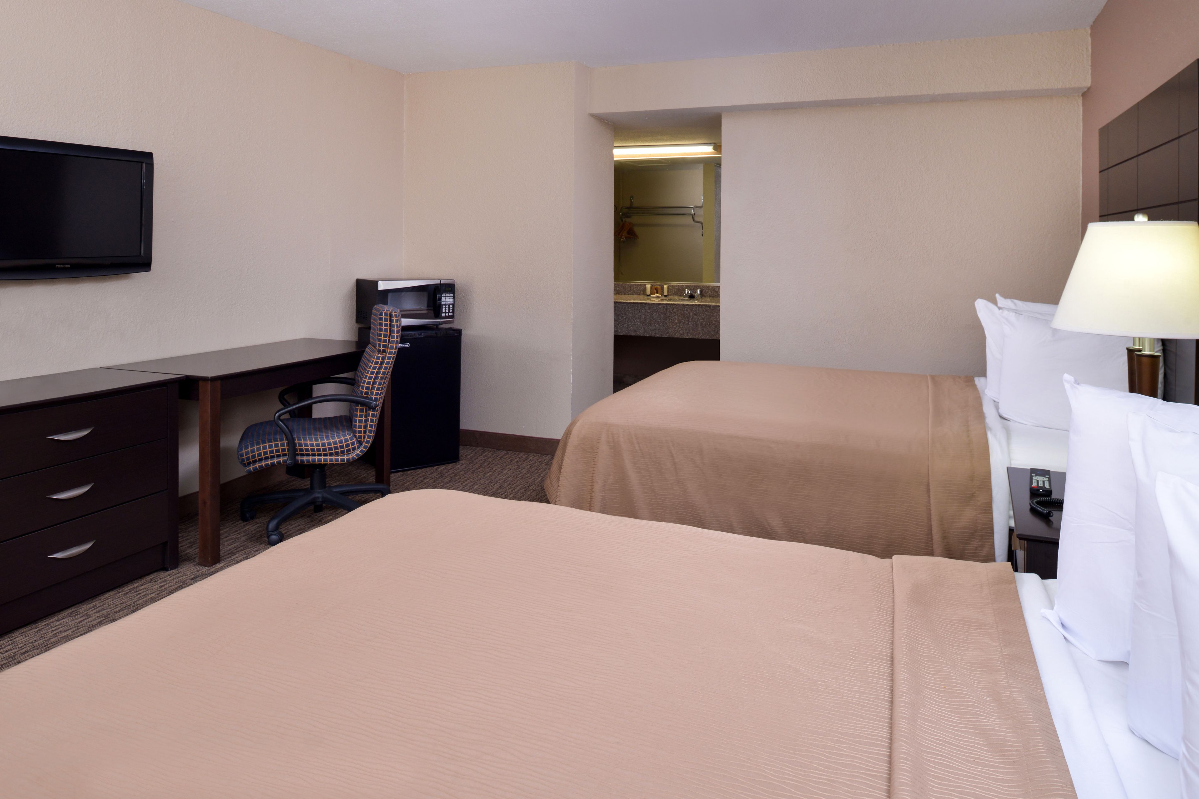 A hotel room with two beds, a desk, a chair, a television, and a bathroom visible through an open door.