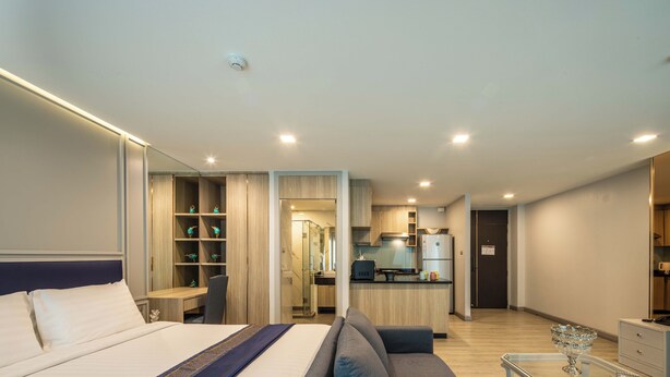 A modern hotel room with a bed, a sofa, a desk, a kitchenette, and a bathroom. - Chaidee Mansion (Bangkok)