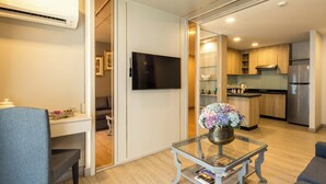 A modern living room with a flat-screen TV, a glass coffee table with a vase, a sofa, and a dining area with a chair. - Chaidee Mansion (Bangkok)