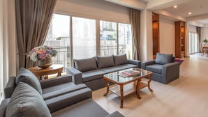 A modern living room with a grey sofa set, a glass coffee table, and a view of the city through large windows. - Chaidee Mansion (Bangkok)