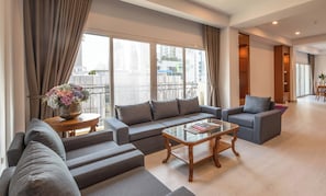 A modern living room with a grey sofa set, a glass coffee table, and a view of the city through large windows. - Chaidee Mansion (Bangkok)