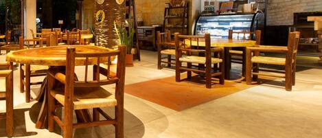 Interior de restaurante con mesas y sillas de madera, un pilar central con obras de arte y una pared de ladrillo con mostrador.