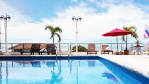 A swimming pool with lounge chairs and umbrellas, surrounded by a colorful building with a tiled roof. - Paloma Del Mar  (Puerto Vallarta)